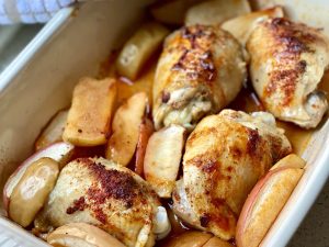 A tray of roasted chicken with apple slices, with paprika sprinkled on top.