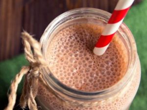 A glass of a chocolatey-looking protein shake made with cacao, with a red and white straw in it.