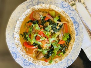 A bowl of Thai red curry with red and green vegetables.