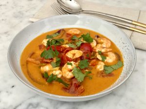 A bowl of prawn stew bursting with colour, topped with herbs.