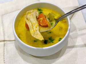 A bowl of Immune-boosting chicken soup with inflammation reducing turmeric, which has given it a wonderful golden colour. A healing soup.