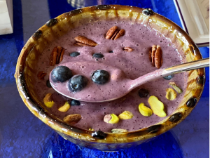 A bowl of banana and blueberry smoothie with nuts and blueberries on top.