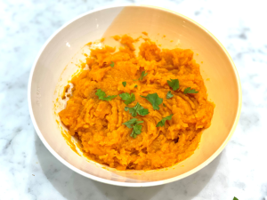 A bowl of sweet potato mash with green herbs on top.
