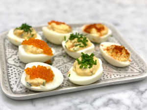 A silver tray with halved eggs topped with a salad filling and trout roe, and herbs sprinkled on top.