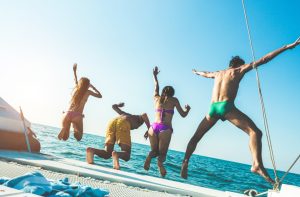 Four people in swimwear jumping off a boat, legs splaying, seen from behind.