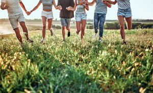 Six people holding hands running in a field, faces not seen.