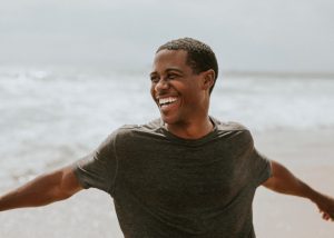 Man on the beach, arms stretched out, laughing. 