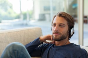 Man on a sofa, smiling, with headphones on.