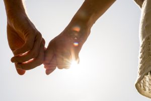 Male and female holding hands, hands seen only, with sunlight shining through.