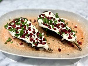 Eggplants halved, filled with tahini dressing with pomegranate seeds and chopped coriander on top on a plate
