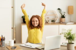 A red-headed girl smiling because she stretches her fascia at the desk