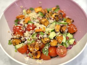 A bowl of salad with tomatoes, quinoa, butternut squash and other vegetables in a pink and cream bowl