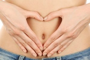 A female stomach shown with a heart shape made by her hands to indicate gut health.