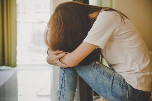 Depressed young female sat holding her knees with her head down