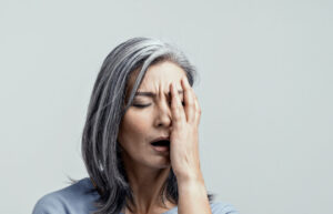 Beautiful Elderly Mature Female Model Touches Face in Headache Upsetted. She Stands in Half-Turn on White Background. Right Side Tonned Portrait.