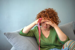 Sad red-haired woman in a green top holding a tape measure crying about her weight