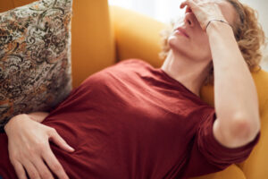 Woman with sinus pain, headache and stomach problems, lying on a couch at home.
