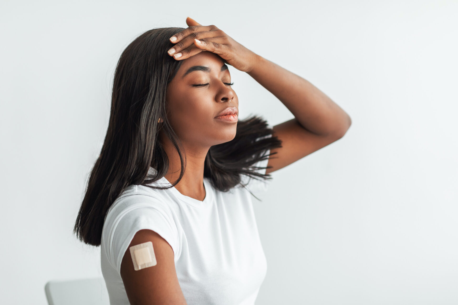 Side Effects To COVID-19 Vaccines. Tired Vaccinated Black Lady With Patch After Coronavirus Antiviral Injection On Arm Touching Forehead, Suffering From Fever, Headache, High Body Temperature