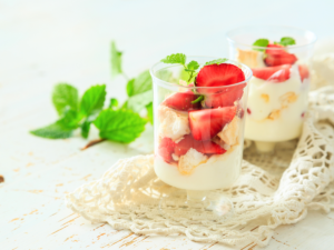 Two glasses with coconut yogurt and strawberries on top. Mint at the side.