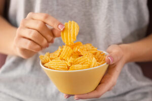 A close up of a bowl of chips being eaten by a lady but only her torso is seen.