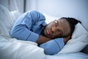 A man in blue pyjamas in lying awake in bed, looking unhappy.