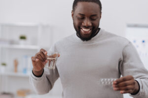 Happy man looking at his pain medication and holding a glass of water.
