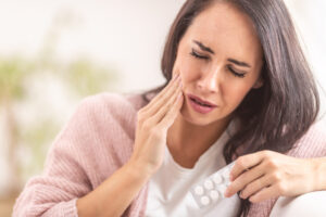 A brown-haired female holds painkillers and indicates tooth pain.