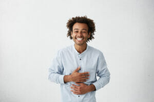 A young man holding his gut and looking happy, indicating the gut and brain health connection.