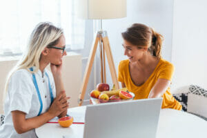 Doctor nutritionist, dietician and female patient on consultation in the office. young smiling female nutritionist in the consultation room. Nutritionist desk with healthy fruit and measuring tape.