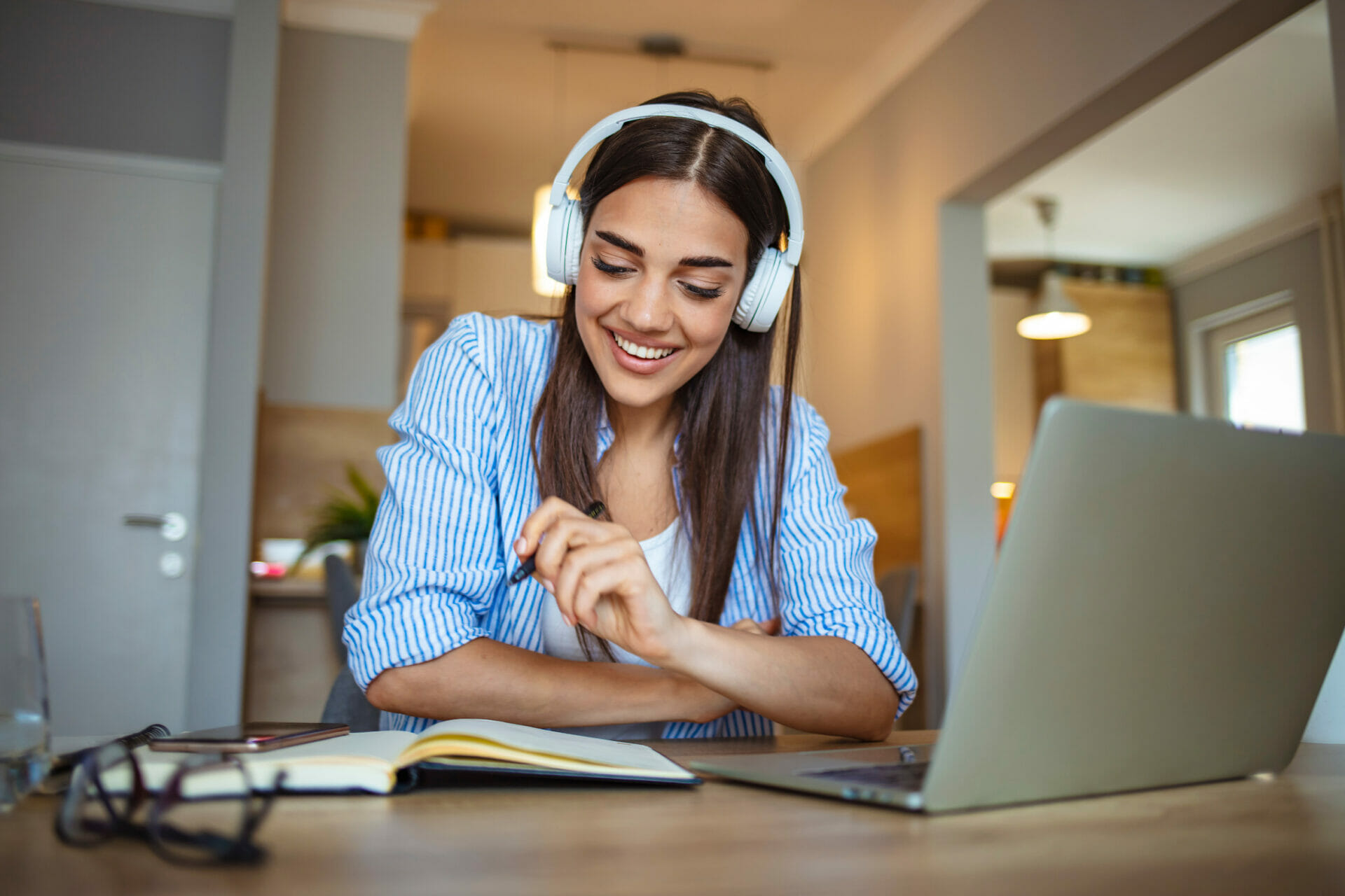 Female student with headphones on learning online, smiling.