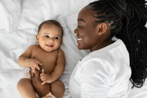 A mother and her baby lying on white sheets, smiling.