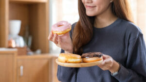 Close up of a woman eating three donuts. Gut health and unhealthy diet. 