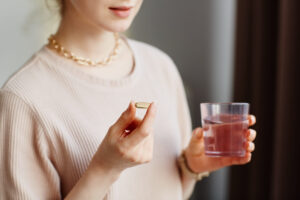 Closeup of young woman holding vitamin capsule while taking supplements with glass of water at home