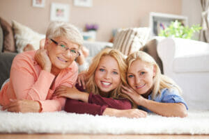 A Grandma, Mother and Daughter lying on the floor next to each other, smiling, looking at the camera.