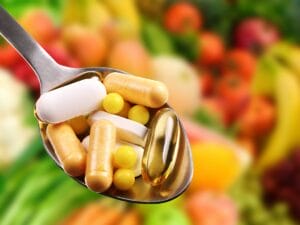rainbow foods background with a spoon in the foreground containing supplements and pills