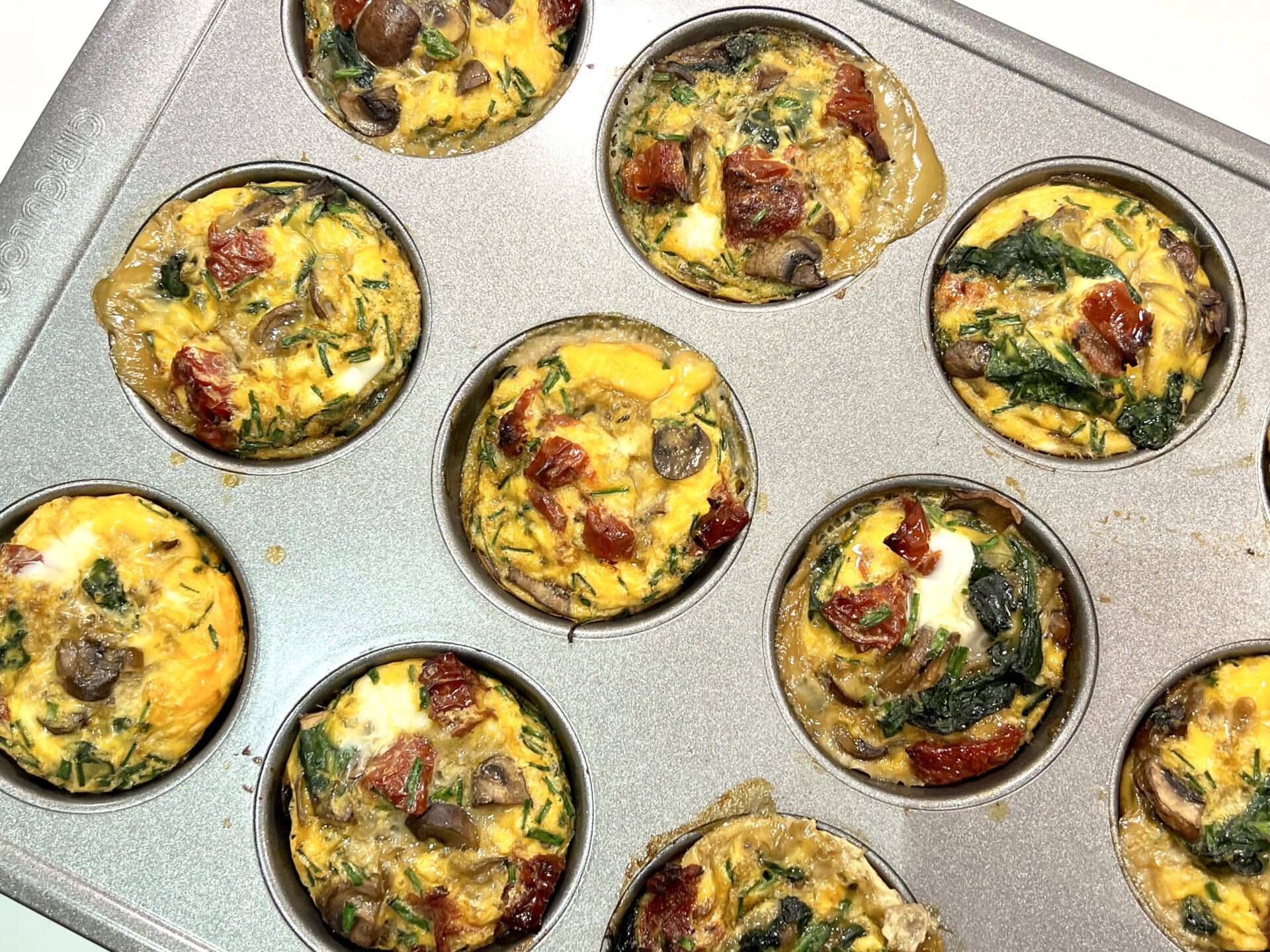 muffin tray with egg muffins filled with mushrooms, spinach and sund-dried tomatoes