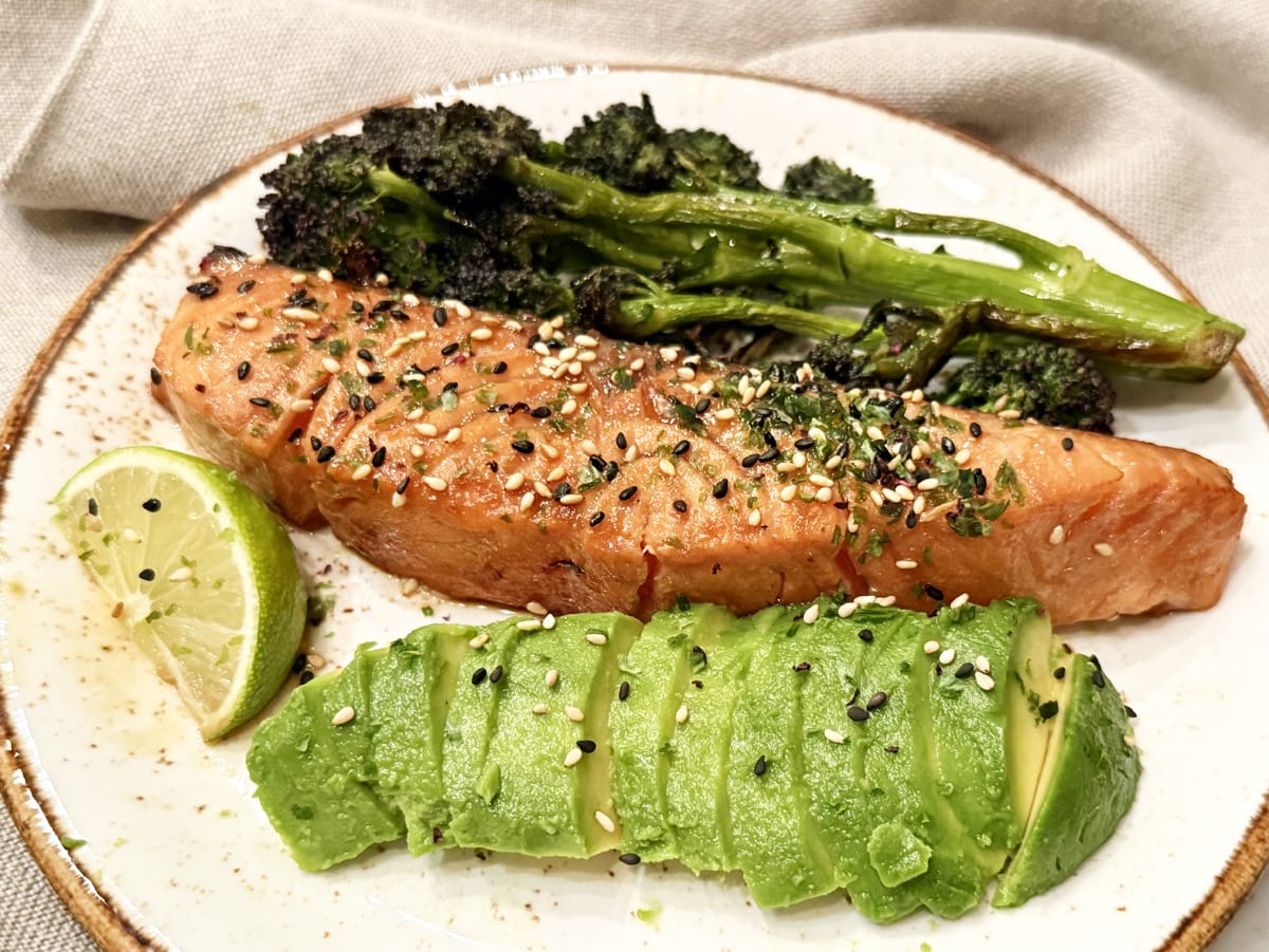 Plate with teriyaki salmon, sliced avocado, tenderstem broccoli and a slice of lime.